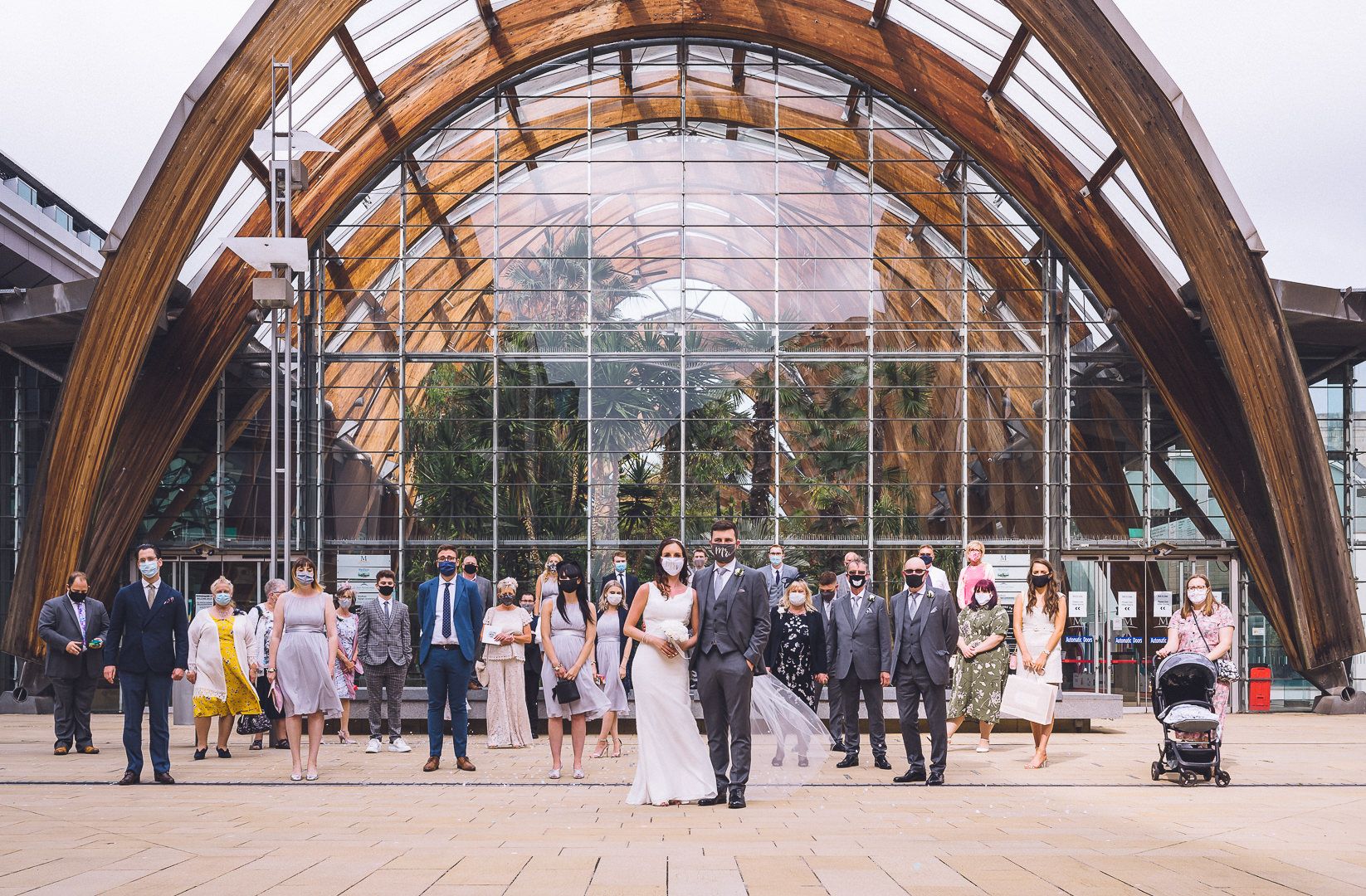 The bride, groom and guests stand apart outside the winter gardens