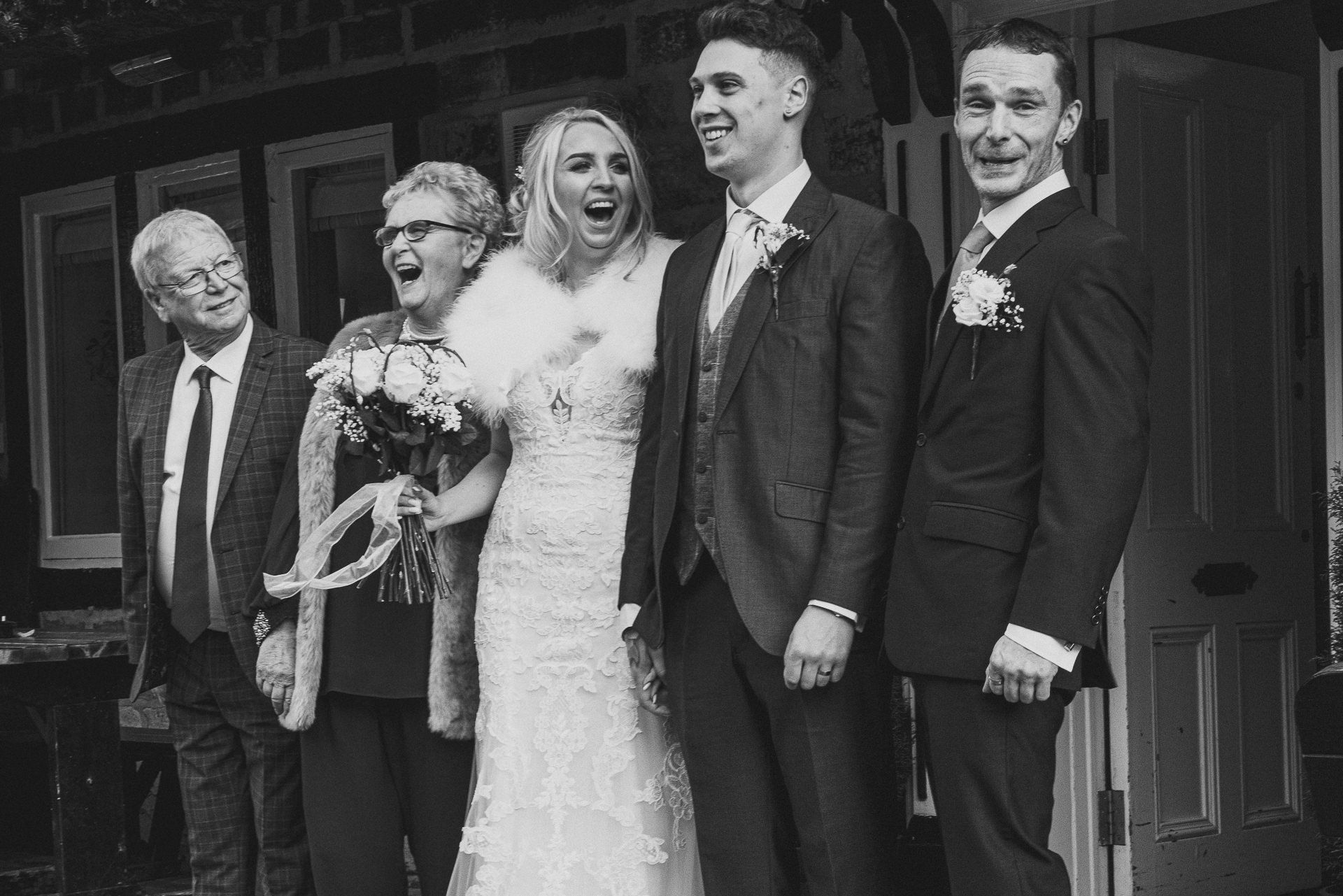 bride is laughing as she poses with her dad, groom and grandparents