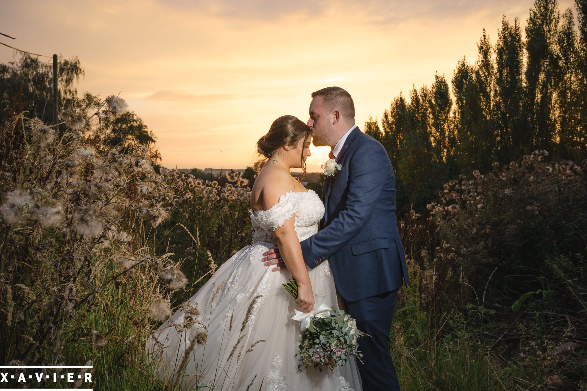 a gentle kiss on the brides head with the sunset behind