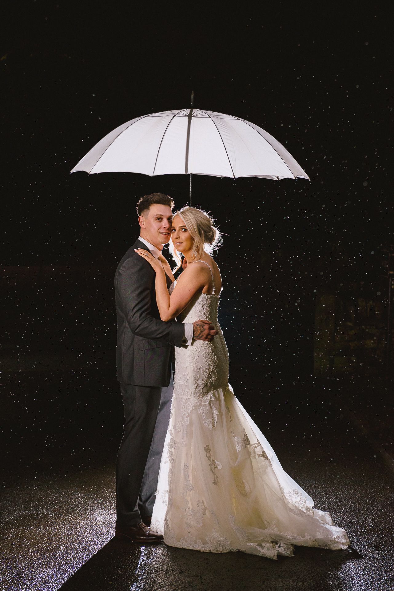 bride and groom stand under a white umbrella at night