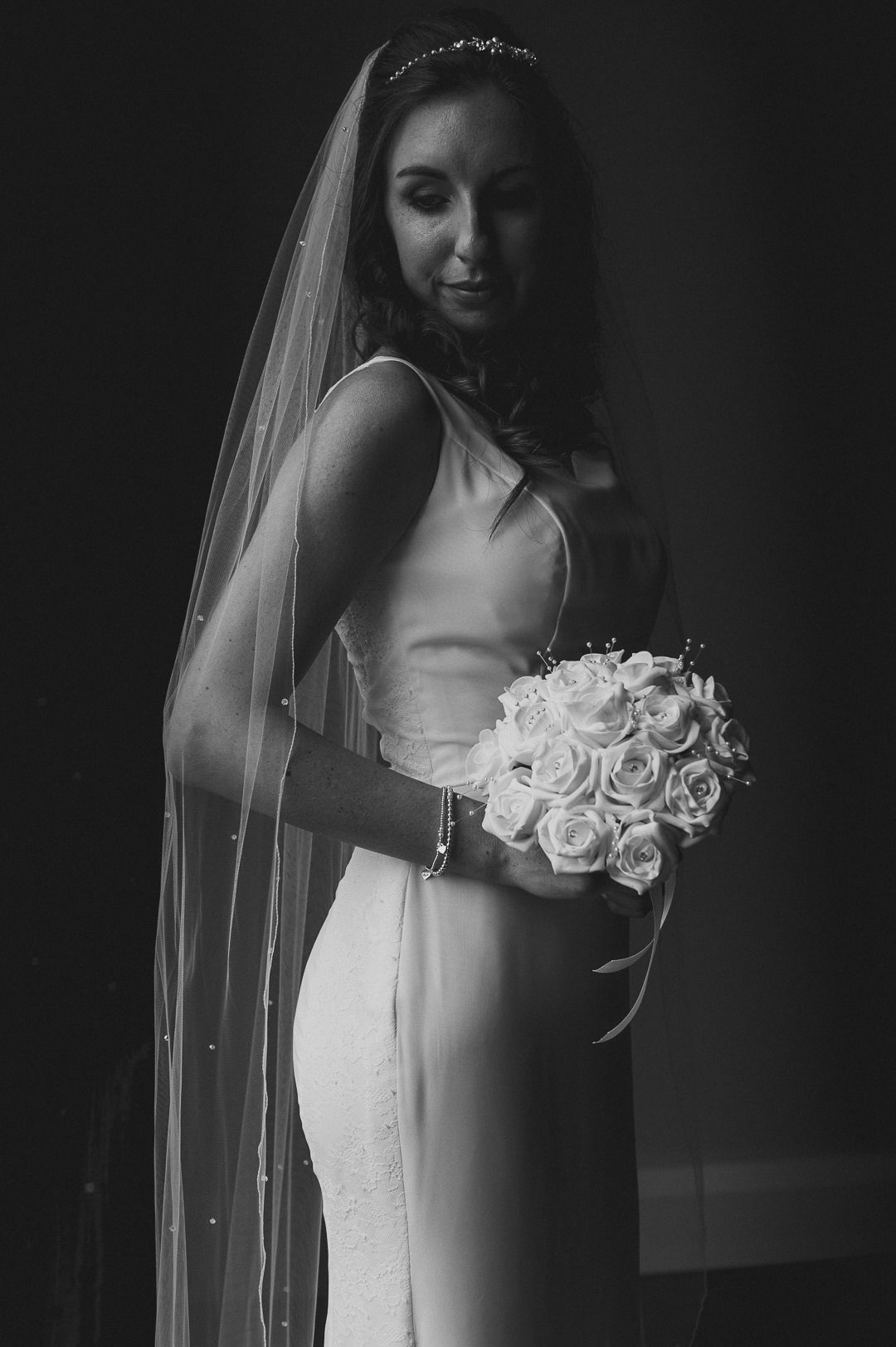 The bride stands in front of the window light and holds her flowers