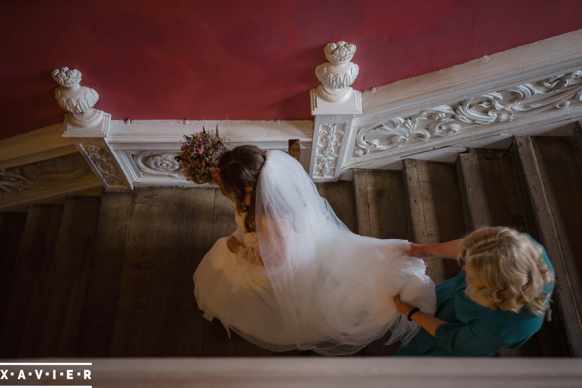 mum holding the brides dress as she walks down the staIRS